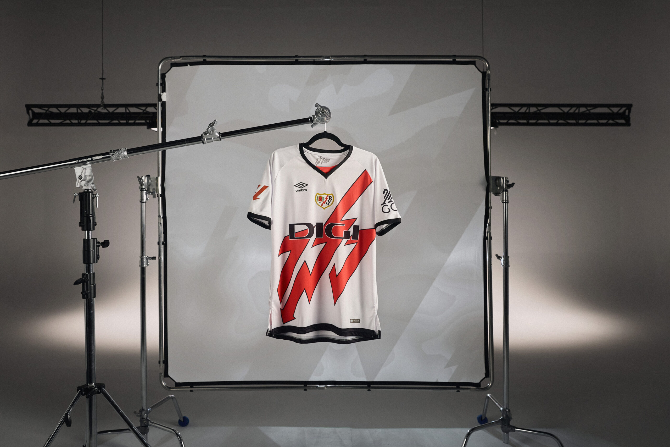 Nueva camiseta de la firma UMBRO para el Rayo Vayecano colgada deuna percha sobre un stand de flas de fotografía cromado con un fondo